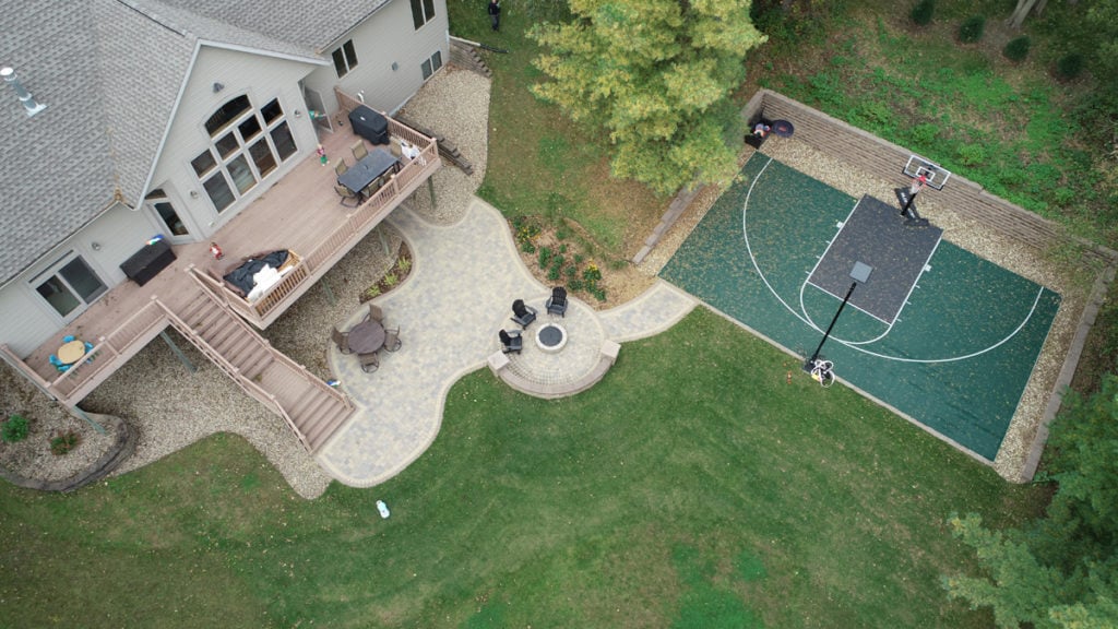 Overhead view of paver patio with fire pit, freestanding wall and walkway leading to basketball court