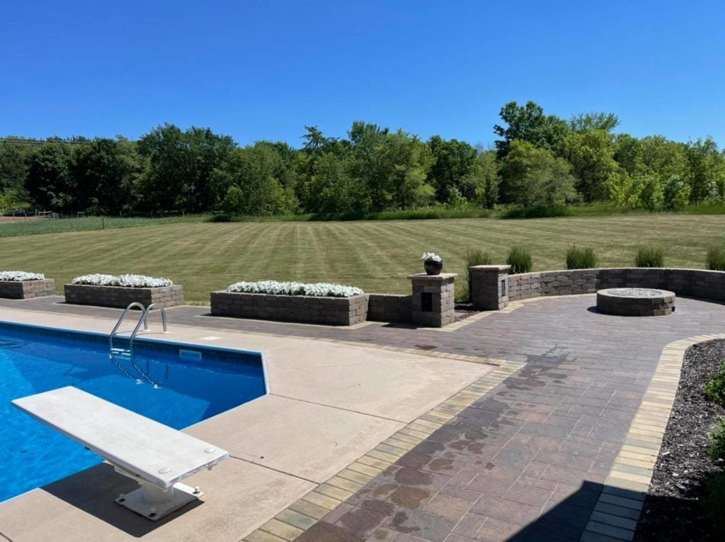 Pavers surrounding a swimming pool with circular patio, fire pit & seating wall