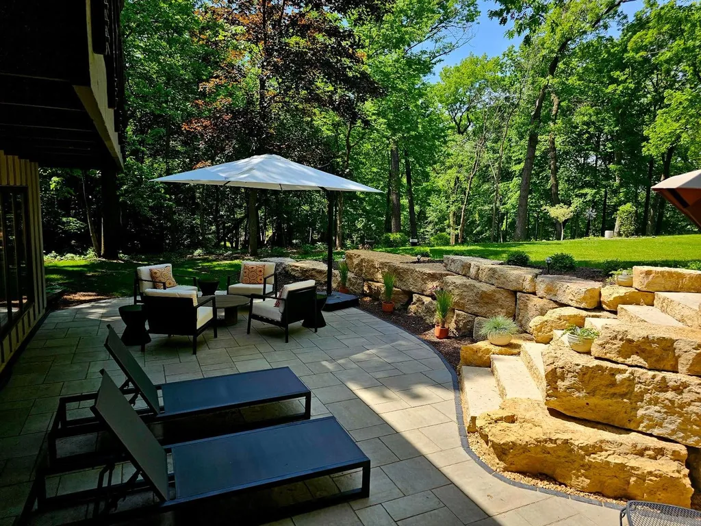 Shaded paver patio with outdoor seating and a terraced natural-stone retaining wall