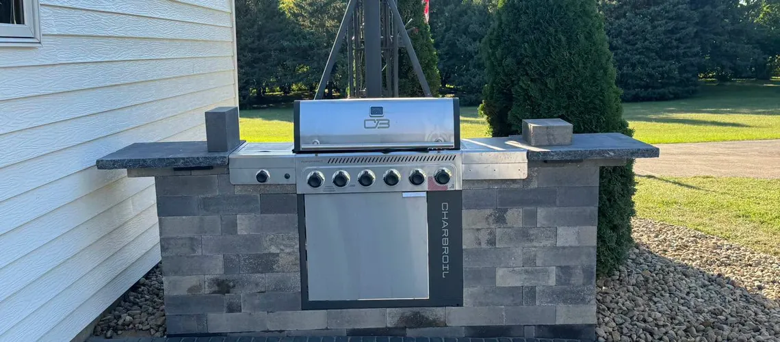 Stainless steel built-in grill set in a stone outdoor kitchen island with dark countertops