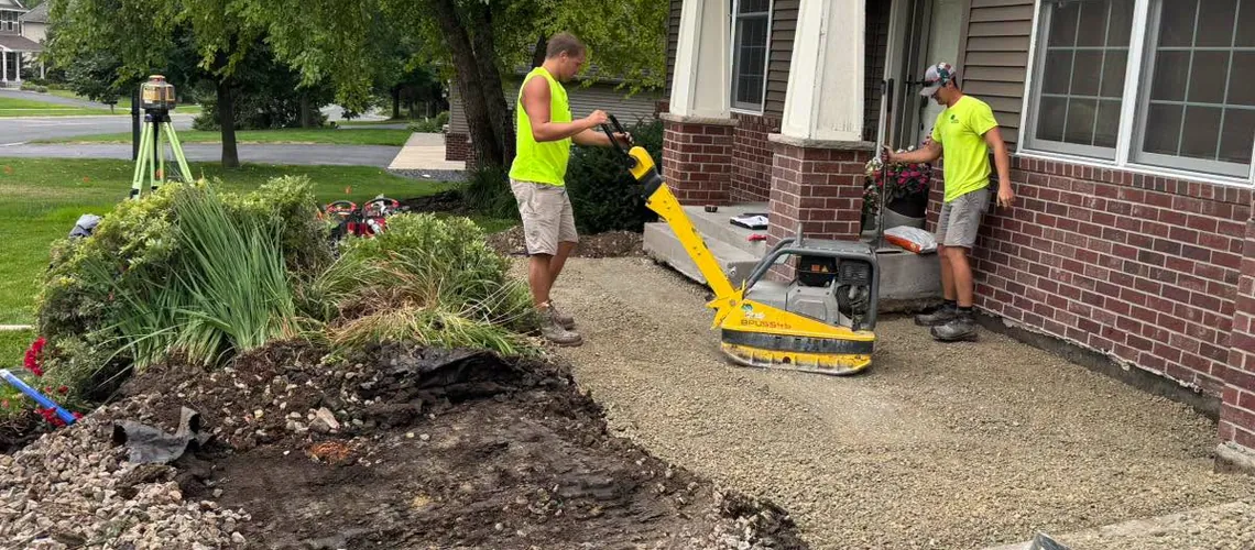 Crew compacting the gravel base for a new front-entry walkway with a plate compactor